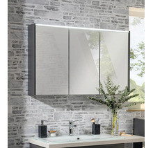 Armoire de toilette à trois portes avec éclairage LED sur un mur à effet pierre au-dessus d'un lavabo.