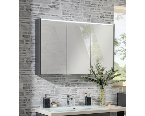 Armoire de toilette à trois portes avec éclairage LED sur un mur à effet pierre au-dessus d'un lavabo.