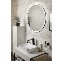 Salle de bain moderne avec miroir LED rond, vasque à poser blanche sur un meuble sous-vasque, robinet noir et mur aspect marbre.