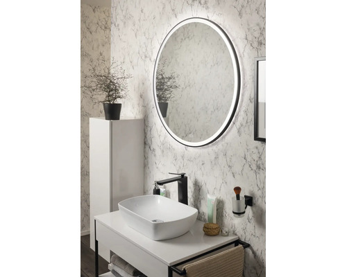 Salle de bain moderne avec miroir LED rond, vasque à poser blanche sur un meuble sous-vasque, robinet noir et mur aspect marbre.