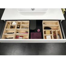 Tiroir de salle de bains organisé avec des inserts modulaires en bois clair contenant divers produits de soin et cosmétiques.