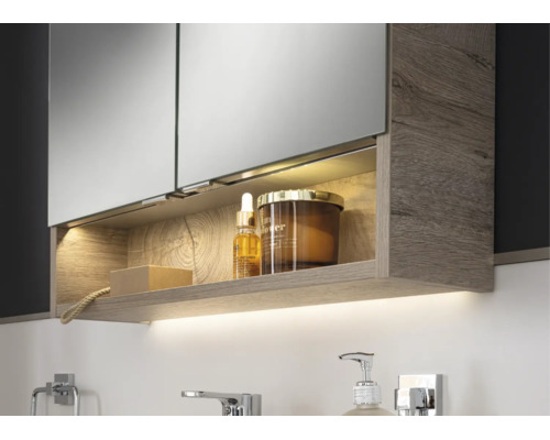 Armoire de toilette moderne avec structure en bois, compartiment éclairé et éclairage indirect sous le meuble dans une salle de bain lumineuse.