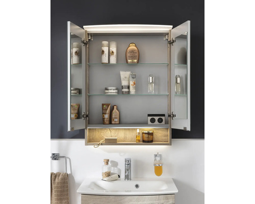 Armoire de toilette ouverte avec éclairage LED, étagères en verre et prise au-dessus d'un lavabo en aspect bois.