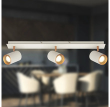 Plafonnier à trois spots avec abat-jour cylindriques blancs et détails cuivrés sur rail dans une salle à manger moderne.