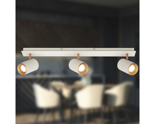 Plafonnier à trois spots avec abat-jour cylindriques blancs et détails cuivrés sur rail dans une salle à manger moderne.