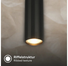 Spot de plafond cylindrique noir avec une structure nervurée distinctive et une source lumineuse blanc chaud allumée.