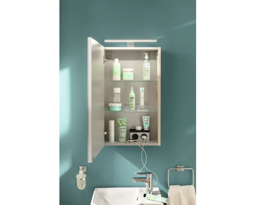 Armoire de toilette lumineuse et organisée avec éclairage LED, étagères en verre et prises intégrées au-dessus d'un lavabo blanc.