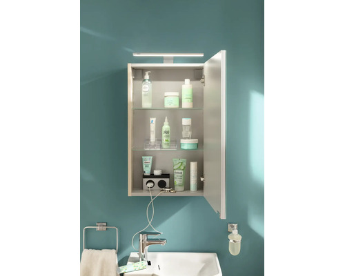 Armoire de toilette ouverte avec éclairage LED, étagères en verre et prise intégrée, installée au-dessus d'un lavabo.