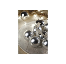 Boules de Noël argentées avec des finitions brillantes et mates sur une assiette, décorées de rubans et d'une guirlande lumineuse.