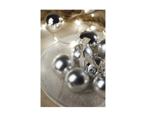 Boules de Noël argentées avec des finitions brillantes et mates sur une assiette, décorées de rubans et d'une guirlande lumineuse.
