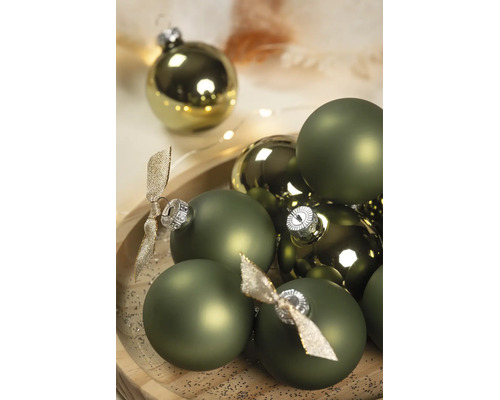 Boules de Noël vertes en versions mates et brillantes avec capuchons argentés et nœuds décoratifs sur un plateau en bois.