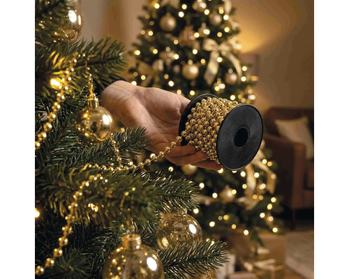 Une main tient une bobine de guirlande de perles pour décorer un sapin de Noël avec des boules et des lumières.