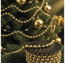 Sapin de Noël décoré d'une guirlande de perles dorées et de boules, avec une bobine de guirlande de perles au premier plan.