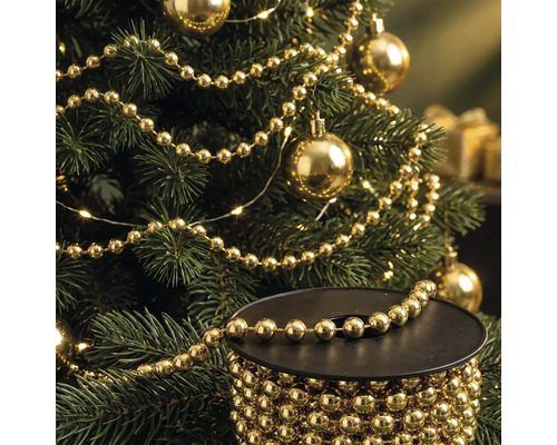 Sapin de Noël décoré d'une guirlande de perles dorées et de boules, avec une bobine de guirlande de perles au premier plan.
