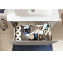 Vue de dessus d'un tiroir ouvert de meuble sous-vasque avec papier toilette, cosmétiques et organiseur pour accessoires de salle de bains.