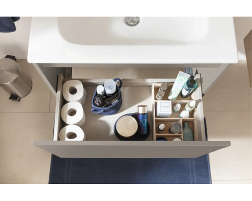 Vue de dessus d'un tiroir ouvert de meuble sous-vasque avec papier toilette, cosmétiques et organiseur pour accessoires de salle de bains.