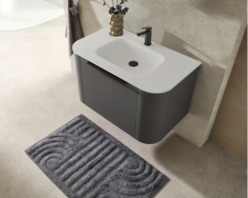 Meuble sous-vasque suspendu moderne avec lavabo blanc, robinetterie noire et tapis de bain gris texturé.