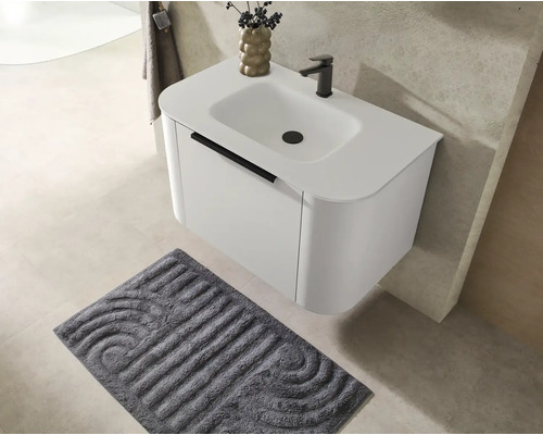 Meuble sous-vasque moderne suspendu avec vasque intégrée, robinetterie noire et tapis de bain assorti dans une salle de bains lumineuse.