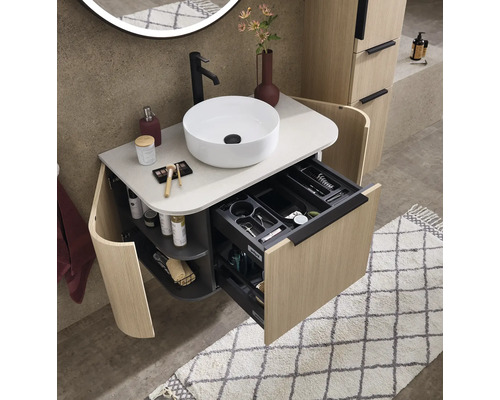 Meuble de salle de bain moderne aspect bois avec vasque ronde, robinet noir et tiroir ouvert avec compartiments de rangement.