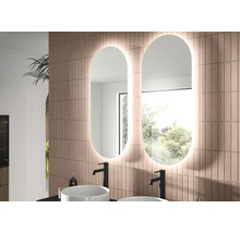 Deux miroirs de salle de bains ovales à LED côte à côte sur un mur carrelé au-dessus de deux vasques à poser blanches avec robinets noirs.