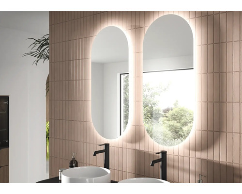 Deux miroirs de salle de bains ovales à LED côte à côte sur un mur carrelé au-dessus de deux vasques à poser blanches avec robinets noirs.