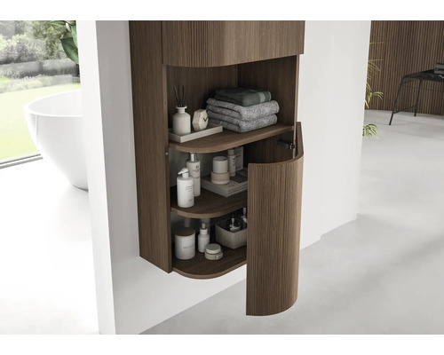 Armoire de toilette suspendue moderne avec rainures verticales en bois et porte arrondie, contenant serviettes et produits de soin.