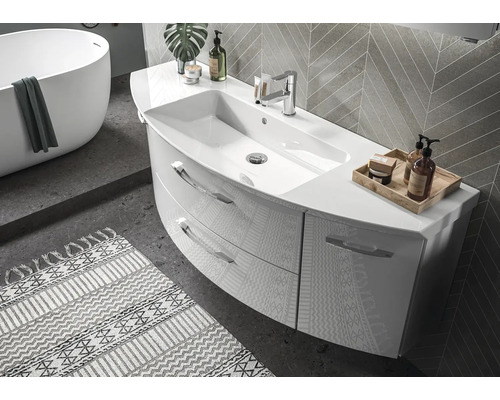 Modernes, helles Badezimmer mit geschwungenem Waschtisch, zwei Schubladen und Armatur. Im Hintergrund freistehende Badewanne und Wandfliesen.