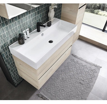 Meuble sous-vasque moderne en aspect chêne clair avec une large vasque blanche et un robinet noir dans une salle de bain lumineuse.