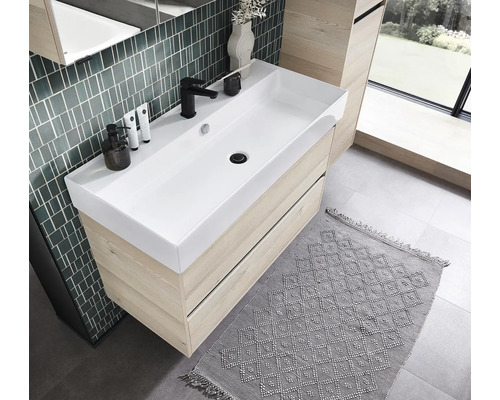 Meuble sous-vasque moderne en aspect chêne clair avec une large vasque blanche et un robinet noir dans une salle de bain lumineuse.