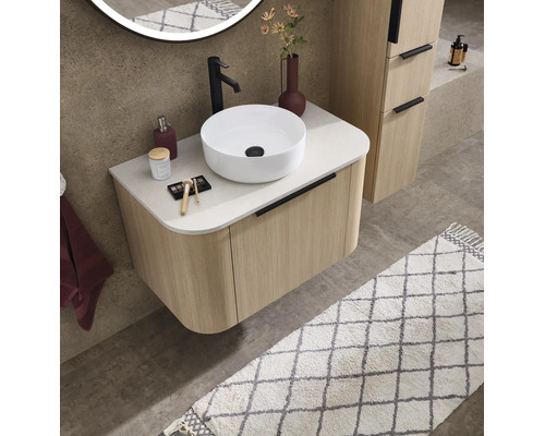 Salle de bains moderne avec meuble sous-lavabo strié aspect bois, vasque à poser blanche, robinet noir et miroir éclairé rond.