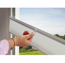 Weiße Plissee-Jalousie am Fenster, die von einer Hand am Griff nach oben geschoben wird.