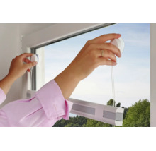 Des mains fixent un store plissé blanc sur une vitre à l'aide de ventouses sans perçage.