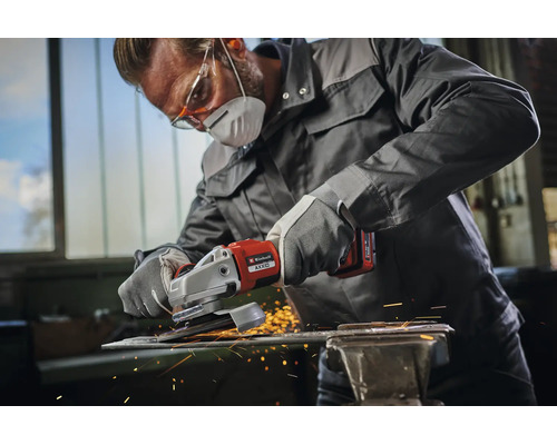 Artisan portant des vêtements de protection utilisant une meuleuse d'angle sans fil Einhell pour travailler une pièce métallique avec étincelles.