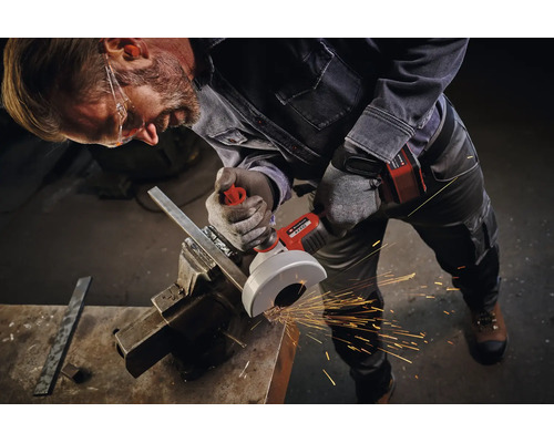 Artisan avec lunettes de protection utilise une meuleuse angulaire sans fil Einhell pour couper du métal dans un étau avec étincelles en atelier