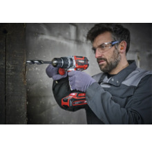 Artisan portant des lunettes de protection perce une poutre en bois avec une perceuse visseuse sans fil Einhell.
