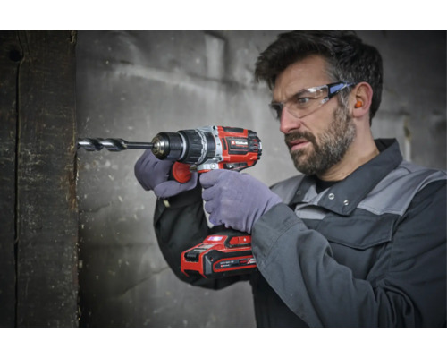 Artisan portant des lunettes de protection perce une poutre en bois avec une perceuse visseuse sans fil Einhell.