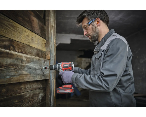 Un artisan utilise une perceuse visseuse sans fil Einhell pour visser dans un mur en bois.
