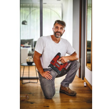 Artisan agenouillé sur un parquet tenant une agrafeuse sans fil Einhell dans un intérieur moderne.