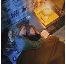 Mutter und Kind liegen im Bett und lesen bei gedimmtem Licht einer Nachttischlampe in einem gemütlichen Kinderzimmer.