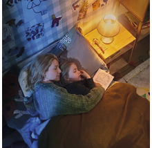 Mutter und Kind lesen abends gemeinsam ein Buch im Kinderzimmer bei gemütlichem Licht der Nachttischlampe.