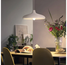 Lampe suspendue moderne au-dessus d une table à manger avec un bouquet de fleurs et de la décoration en arrière-plan dans un espace lumineux.