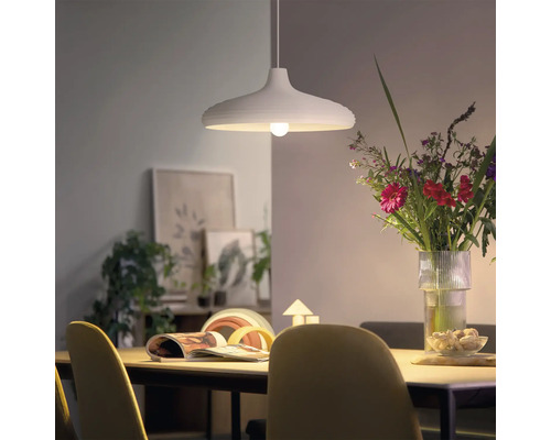 Lampe suspendue moderne au-dessus d une table à manger avec un bouquet de fleurs et de la décoration en arrière-plan dans un espace lumineux.