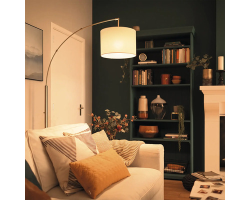 Lampadaire moderne avec abat-jour en tissu à côté d'un canapé dans un salon confortable avec une étagère sombre et une cheminée.