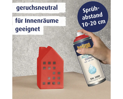 Eine Hand sprüht mit einer geruchsneutralen Belton Aqua Colours Sprühdose in Feuerrot auf ein kleines dekoratives Haus aus Keramik.