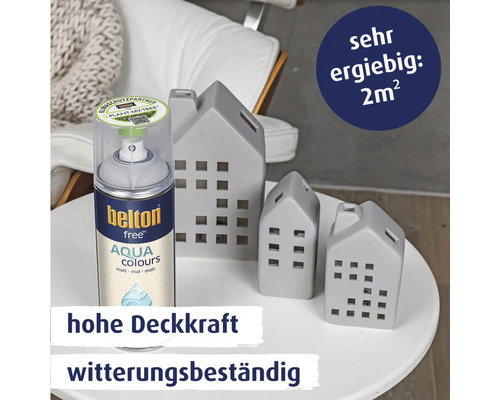 Eine Spraydose Belton Free Aqua Colours Lack mit drei dekorativen Häuserfiguren auf einem Tisch mit Informationen zu Ergiebigkeit und Deckkraft.
