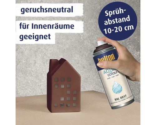 Eine Hand hält eine Sprühdose Belton Aqua Colours matt RAL 8017 über einem dekorativen Hausmodell zur Anwendung im Innenbereich.