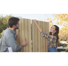 Un couple assemble ensemble en extérieur un panneau d'intimité à lames verticales en bois pour le jardin.