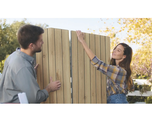 Un couple assemble ensemble en extérieur un panneau d'intimité à lames verticales en bois pour le jardin.
