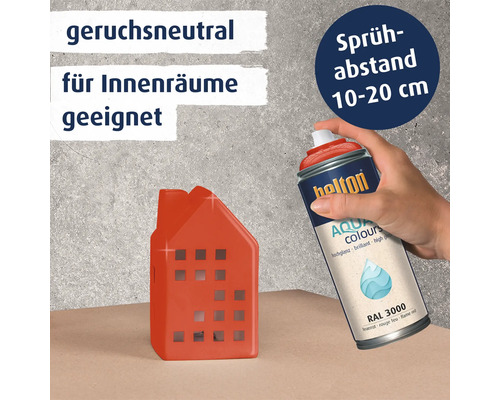 Eine Hand sprüht mit einer Belton Aqua Colors Lackspraydose in Feuerrot auf ein kleines dekoratives Haus aus Keramik.