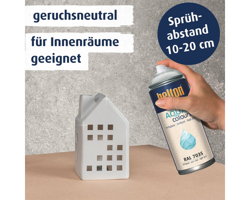 Eine Hand sprüht mit Helton Aqua Colours Lack in lichtgrau RAL 7035 auf ein weißes Deko Haus. Produktinformationen für Innenräume.